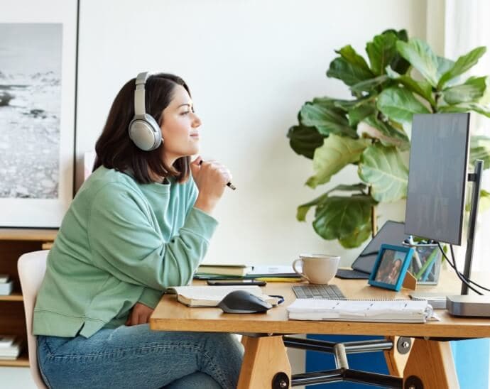 Femme portant un casque audio, tenant un crayon et regardant un écran de PC